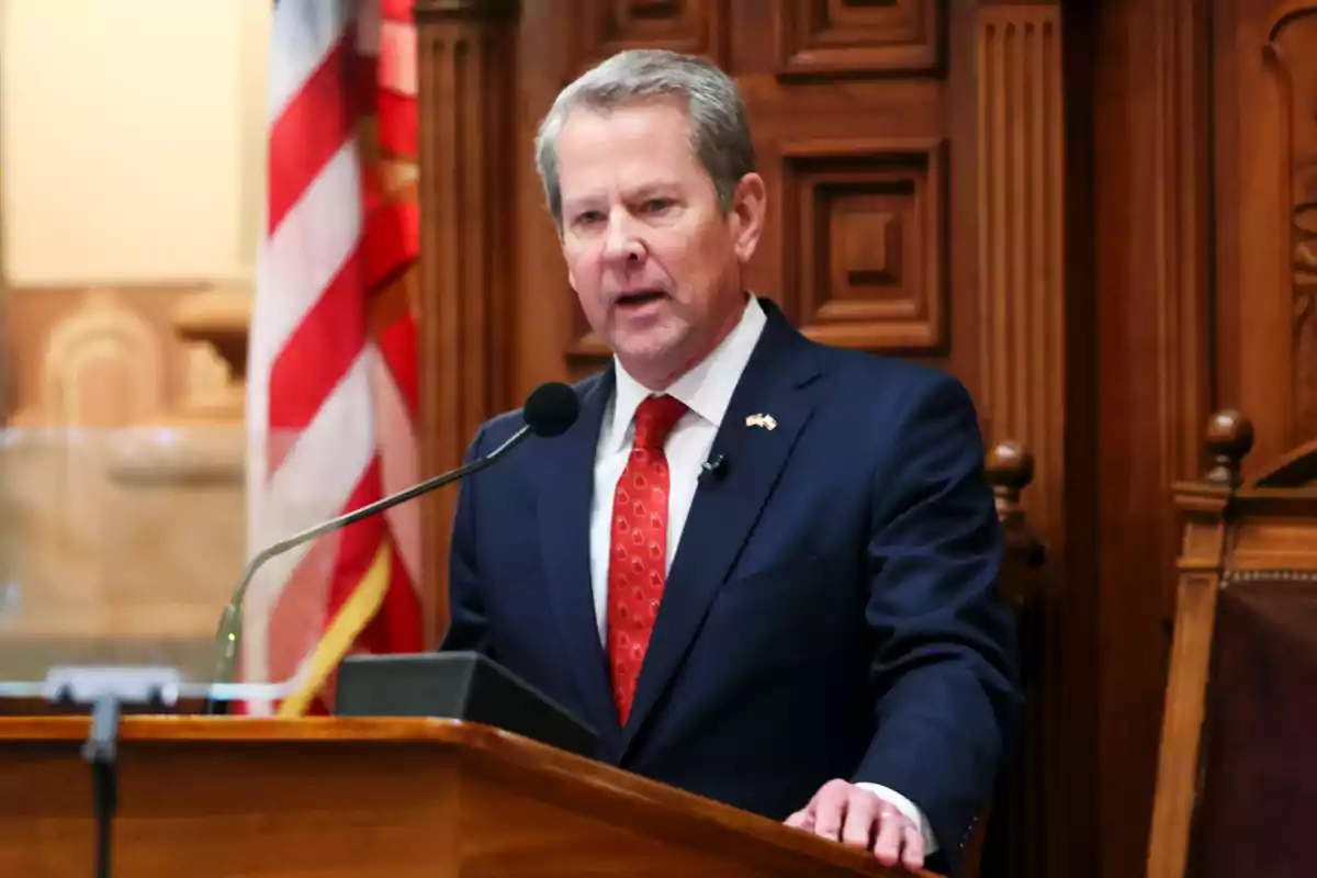 Man in a blue suit and red tie speaking at a podium with a United States flag in the background Man in a blue suit and red tie speaking at a podium with a United States flag in the background