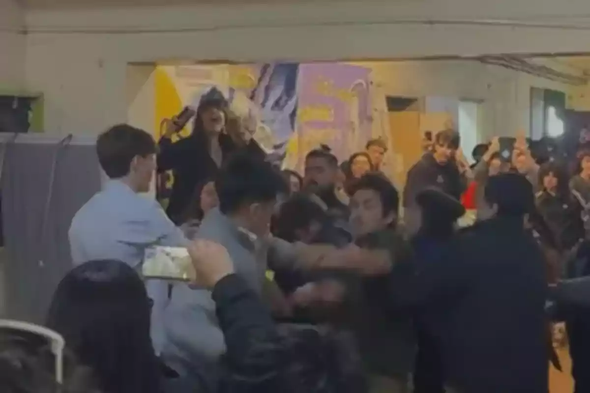 Several people are fighting in an enclosed space while a crowd watches and records with their cell phones. Several people are fighting in an enclosed space while a crowd watches and records with their cell phones.