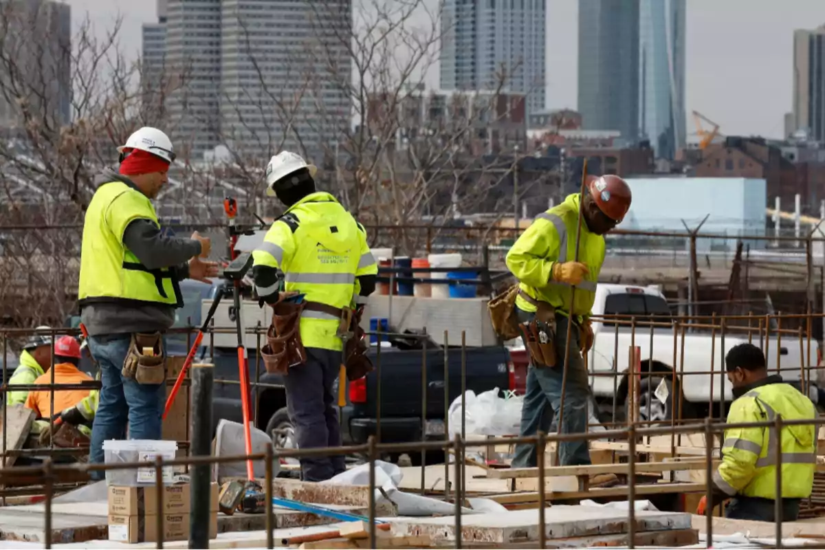 Trabajadores de la construcción con chalecos y cascos de seguridad laboran en una obra urbana con edificios altos al fondo Trabajadores de la construcción con chalecos y cascos de seguridad laboran en una obra urbana con edificios altos al fondo