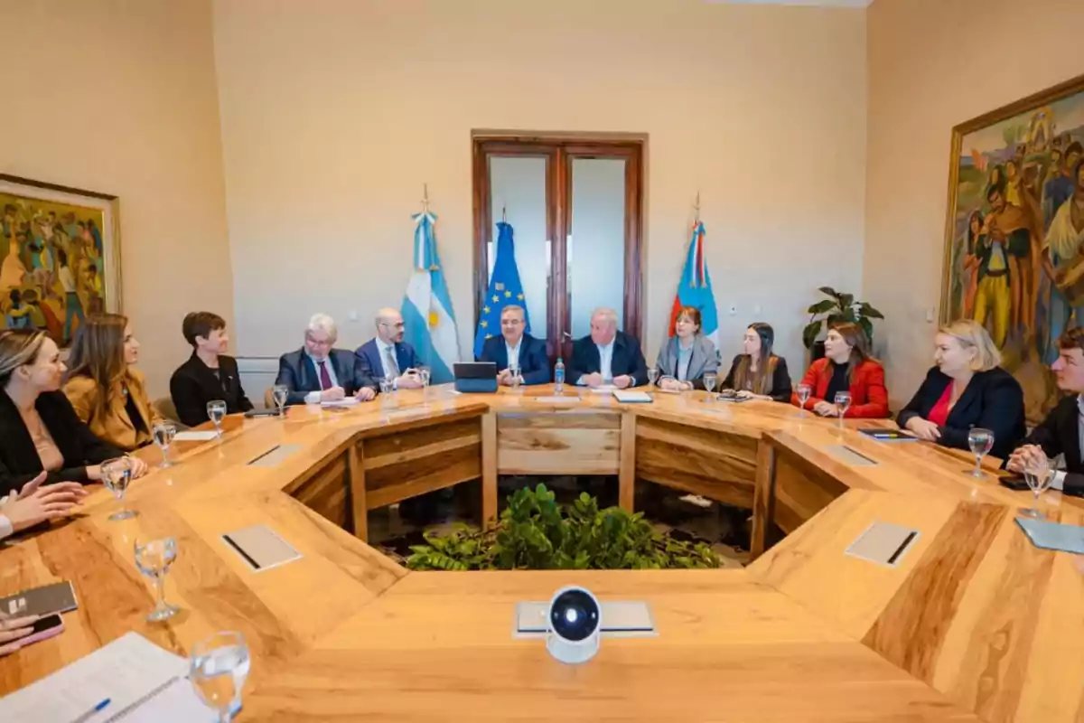 Meeting of several people sitting around a wooden table in a conference room with flags and paintings on the walls