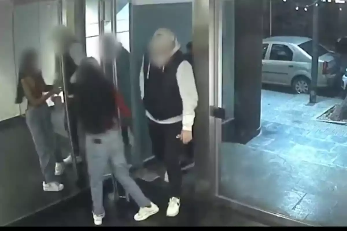 Varias personas con los rostros difuminados están entrando o saliendo de un edificio a través de una puerta de vidrio, mientras afuera se observa un automóvil estacionado. Varias personas con los rostros difuminados están entrando o saliendo de un edificio a través de una puerta de vidrio, mientras afuera se observa un automóvil estacionado.