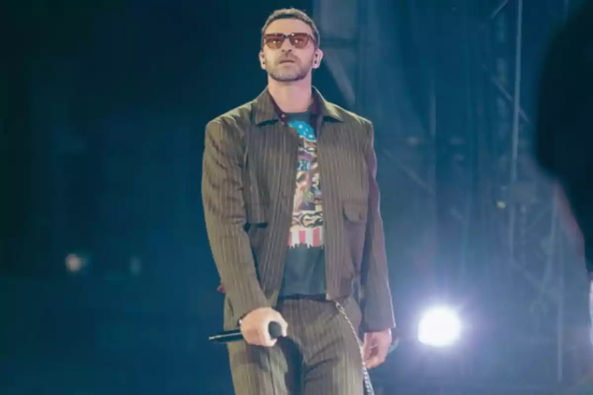 Man with sunglasses and a microphone in his hand on a lit stage