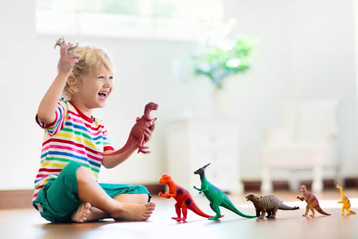 Niño sonriente jugando en el suelo con varios dinosaurios de juguete en una habitación iluminada Niño sonriente jugando en el suelo con varios dinosaurios de juguete en una habitación iluminada