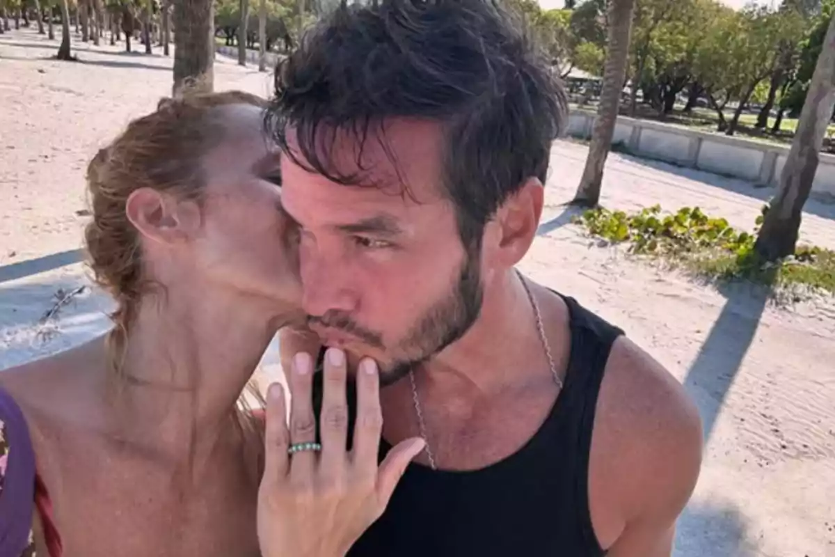 Pareja abrazada en la playa mientras la mujer besa al hombre en la mejilla Pareja abrazada en la playa mientras la mujer besa al hombre en la mejilla