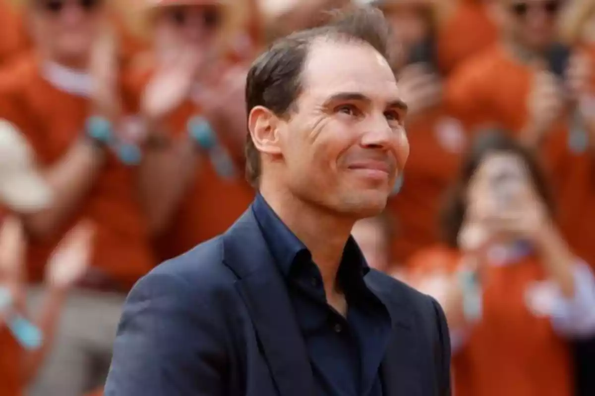 Hombre sonriente con saco oscuro en un evento con público de fondo desenfocado