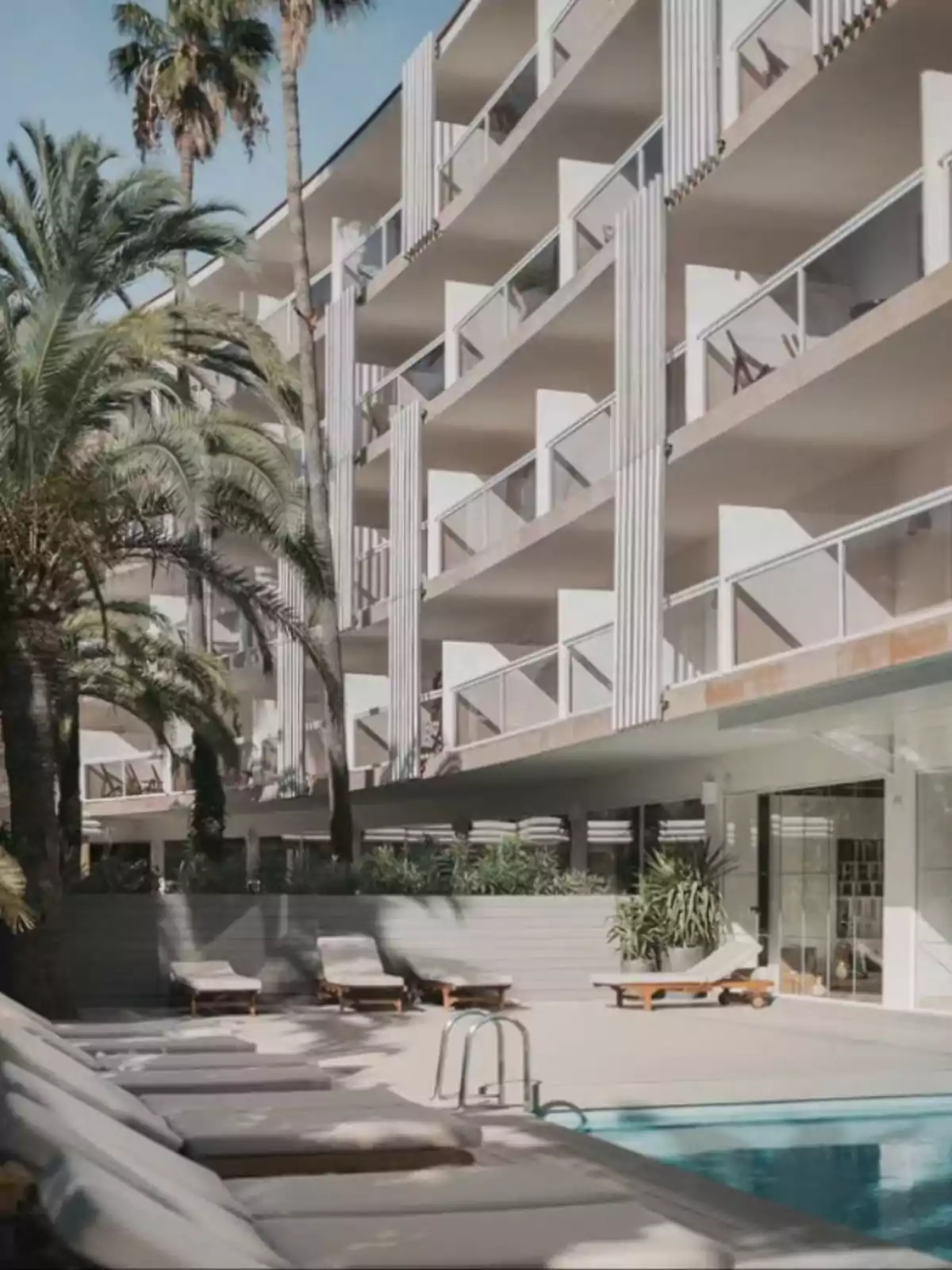 Hotel moderno con balcones privados rodeado de palmeras y una piscina con tumbonas en primer plano Hotel moderno con balcones privados rodeado de palmeras y una piscina con tumbonas en primer plano