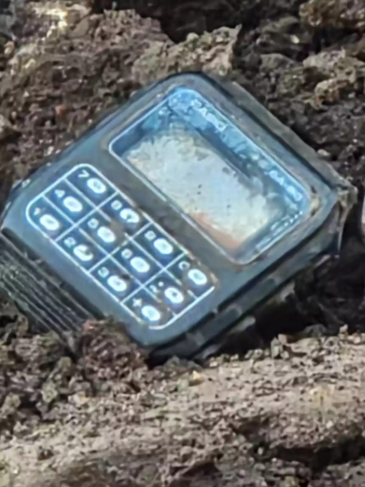 An old mobile phone partially covered with dirt An old mobile phone partially covered with dirt