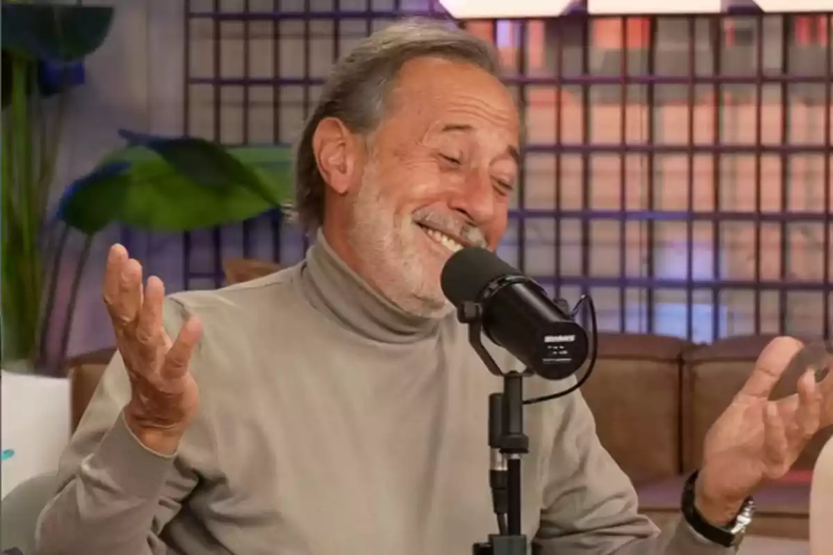Hombre mayor sonriendo y encogiéndose de hombros mientras habla frente a un micrófono en un estudio de grabación Hombre mayor sonriendo y encogiéndose de hombros mientras habla frente a un micrófono en un estudio de grabación