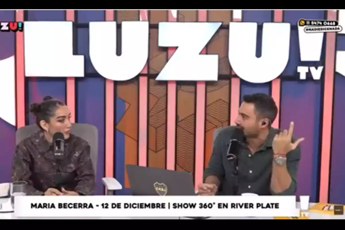 Dos personas conversan en un estudio de radio con el logo de Luzu TV de fondo y un anuncio en la parte inferior sobre un show de María Becerra el 12 de diciembre en River Plate
