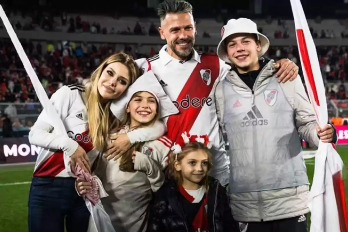 Familia sonriente vestida con camisetas de River Plate posando en un estadio de fútbol Familia sonriente vestida con camisetas de River Plate posando en un estadio de fútbol