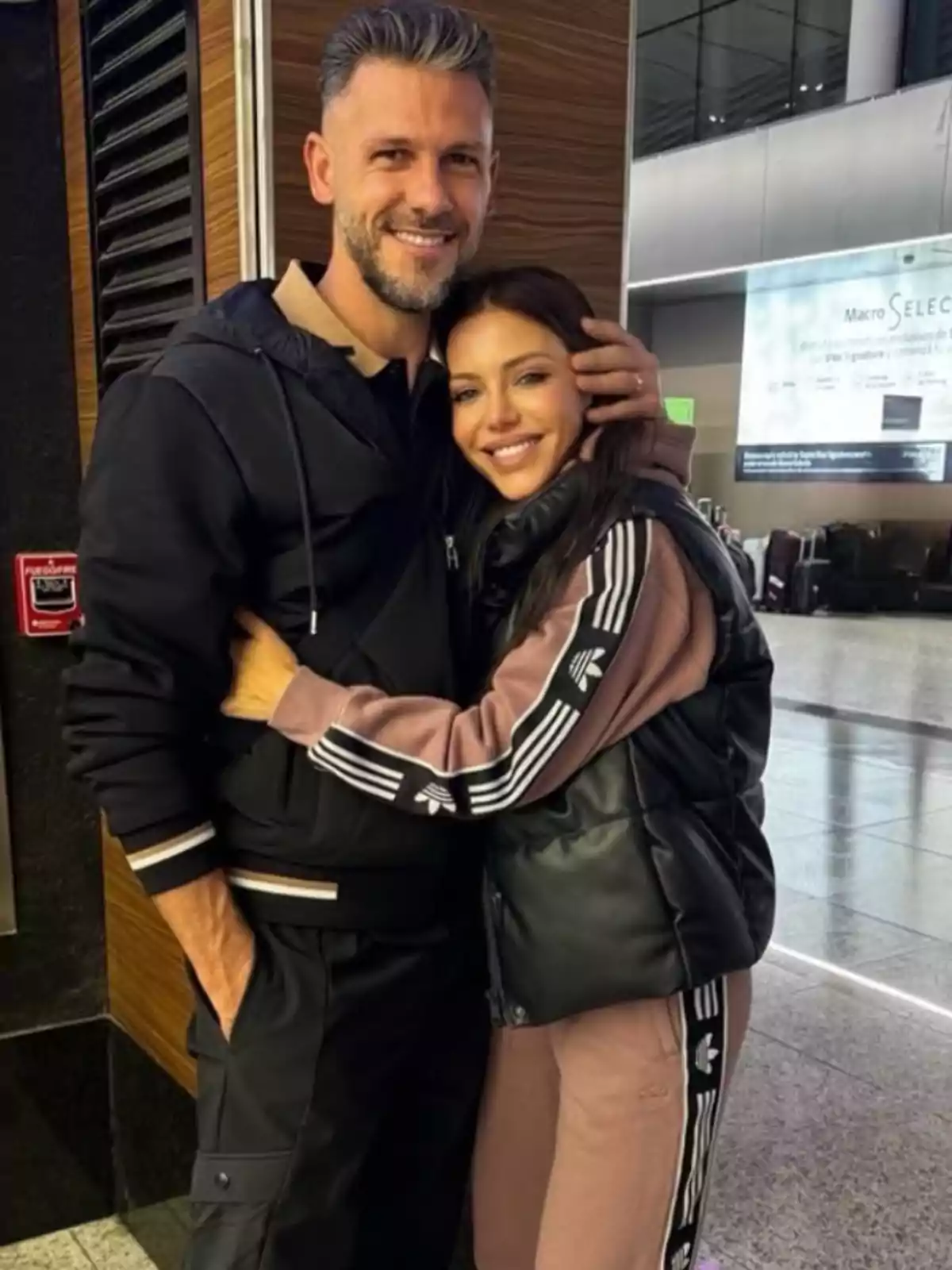 Pareja abrazándose y sonriendo en lo que parece ser un aeropuerto, ambos vestidos con ropa deportiva. Pareja abrazándose y sonriendo en lo que parece ser un aeropuerto, ambos vestidos con ropa deportiva.