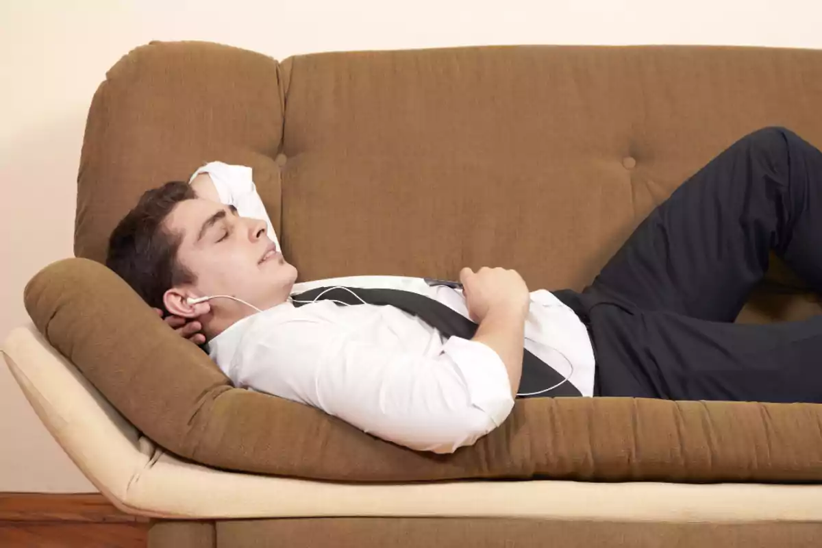 Young man in a white jersey and black tie relaxing on a brown sofa while listening to music with headphones Young man in a white jersey and black tie relaxing on a brown sofa while listening to music with headphones