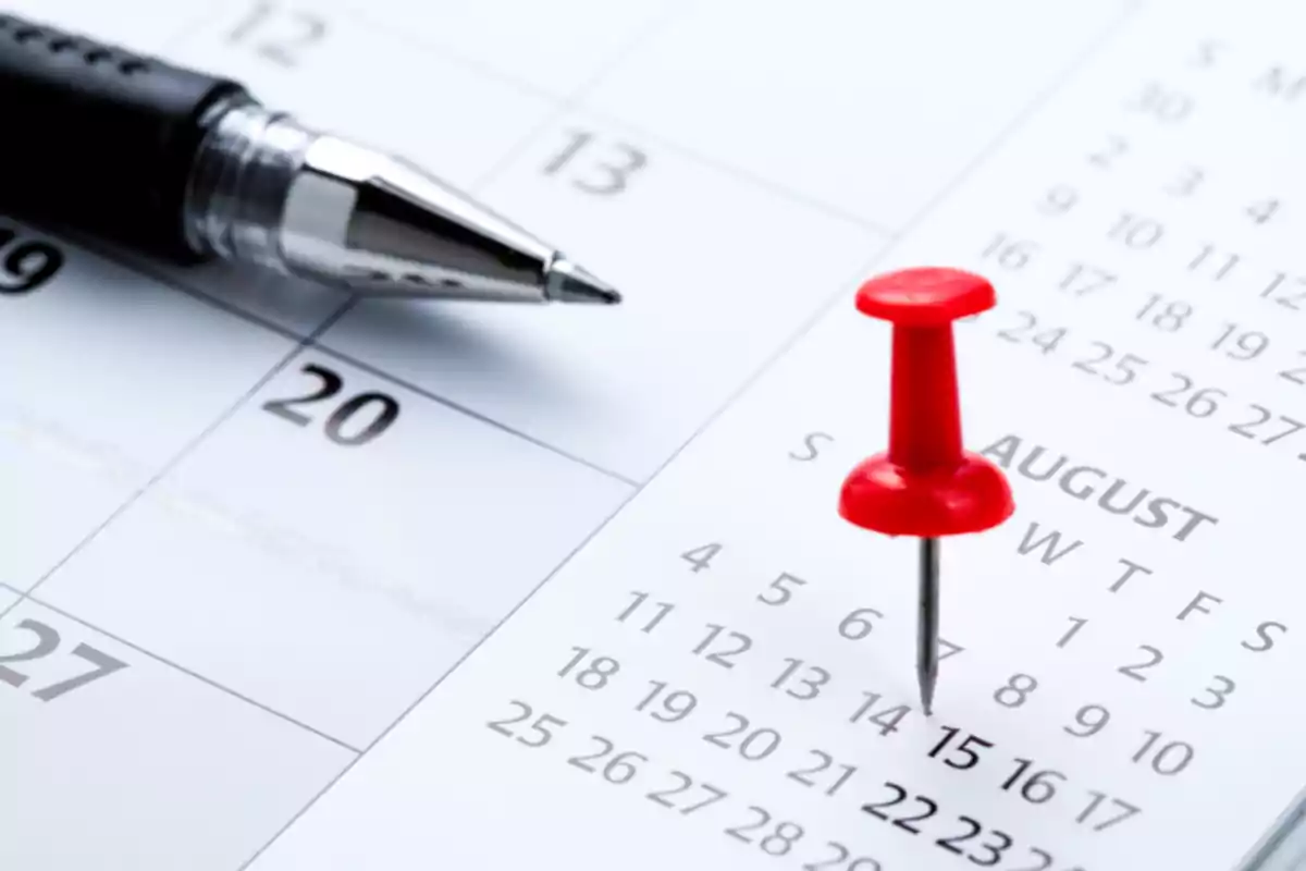 Close-up of a calendar with a black pen and a red pushpin marking a date in August
