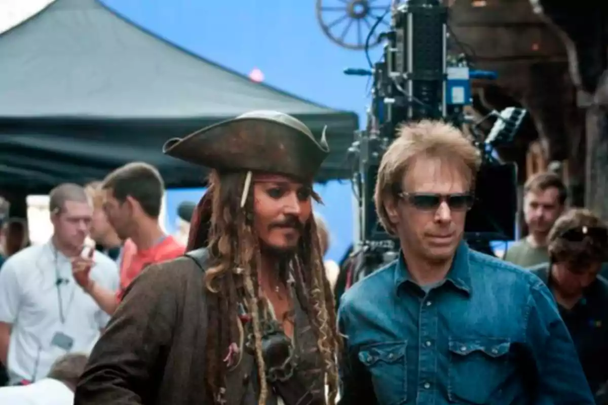Un hombre disfrazado de pirata junto a otro hombre con gafas de sol en un set de filmación rodeados de equipo técnico y cámaras Un hombre disfrazado de pirata junto a otro hombre con gafas de sol en un set de filmación rodeados de equipo técnico y cámaras