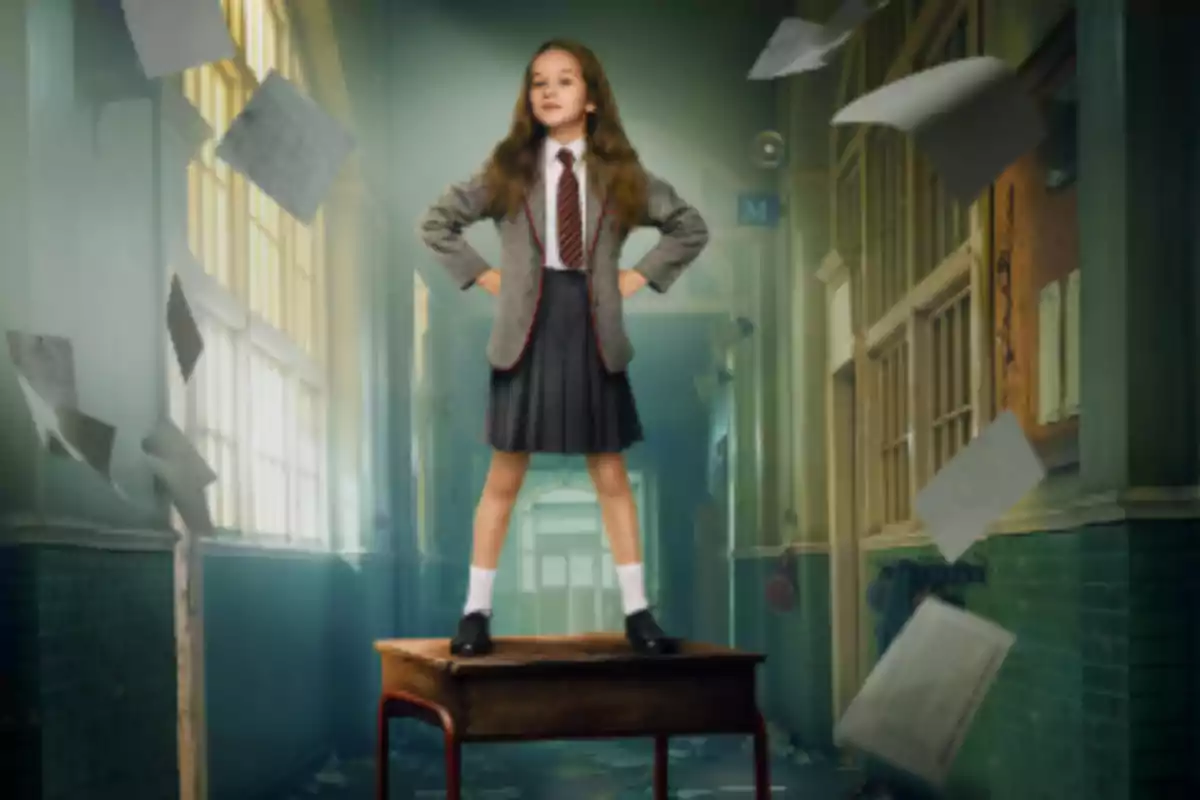 Niña con uniforme escolar de pie sobre un escritorio en un pasillo mientras hojas de papel vuelan a su alrededor Niña con uniforme escolar de pie sobre un escritorio en un pasillo mientras hojas de papel vuelan a su alrededor