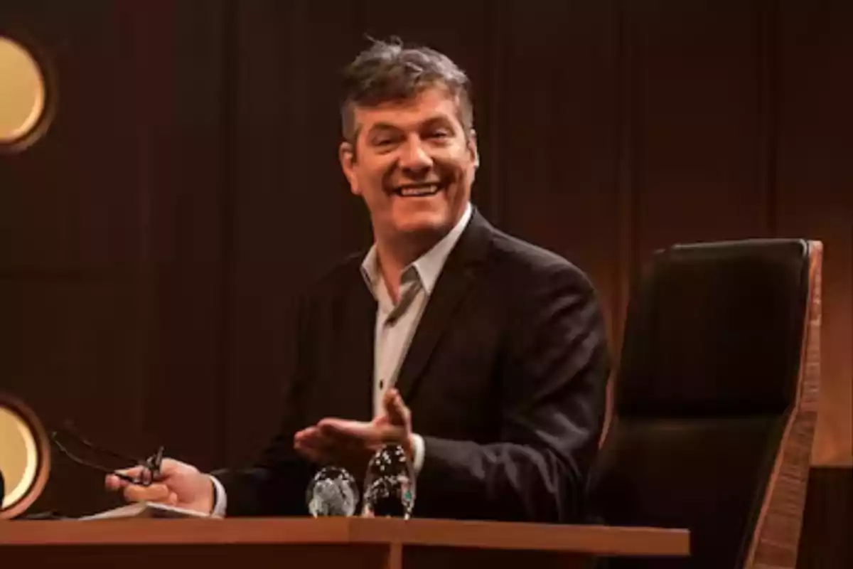 Man in a dark suit smiling while sitting at a wooden desk Man in a dark suit smiling while sitting at a wooden desk
