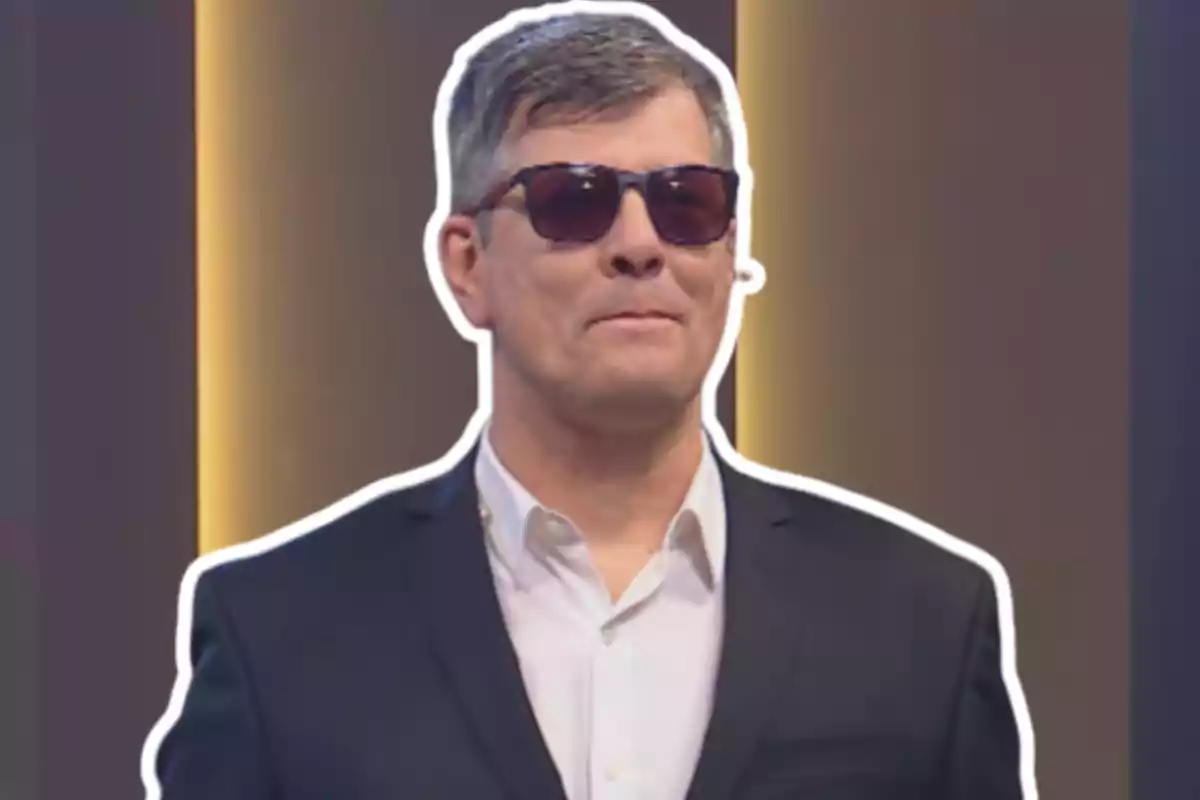 Short-haired man with dark glasses and a dark suit against a background with vertical lights