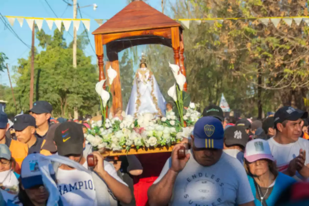 People take part in a religious procession carrying an image of the Virgin decorated with white flowers and surrounded by devotees. People take part in a religious procession carrying an image of the Virgin decorated with white flowers and surrounded by devotees.