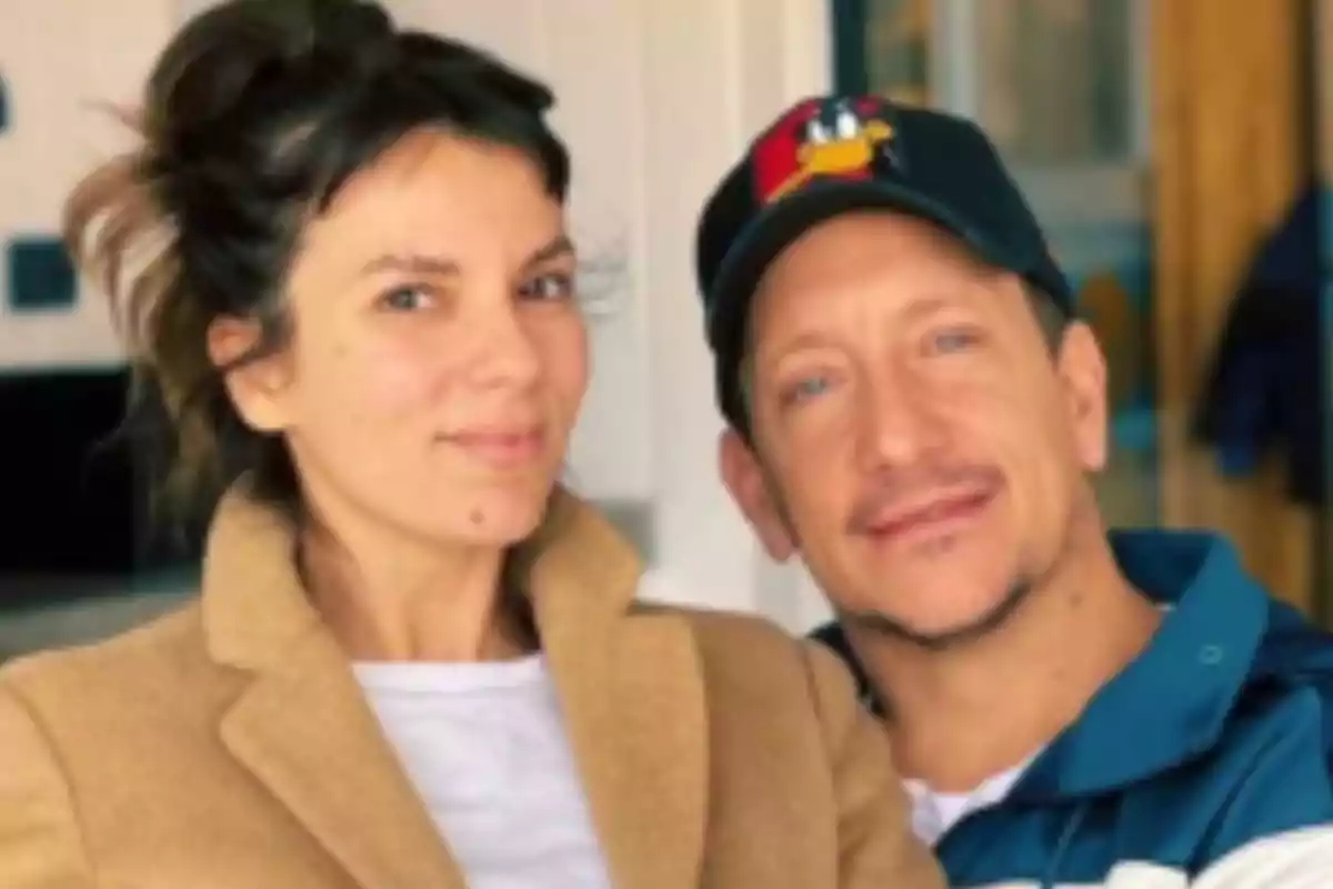Una mujer con abrigo beige y un hombre con gorra negra posan juntos y sonríen en un ambiente interior iluminado. Una mujer con abrigo beige y un hombre con gorra negra posan juntos y sonríen en un ambiente interior iluminado.