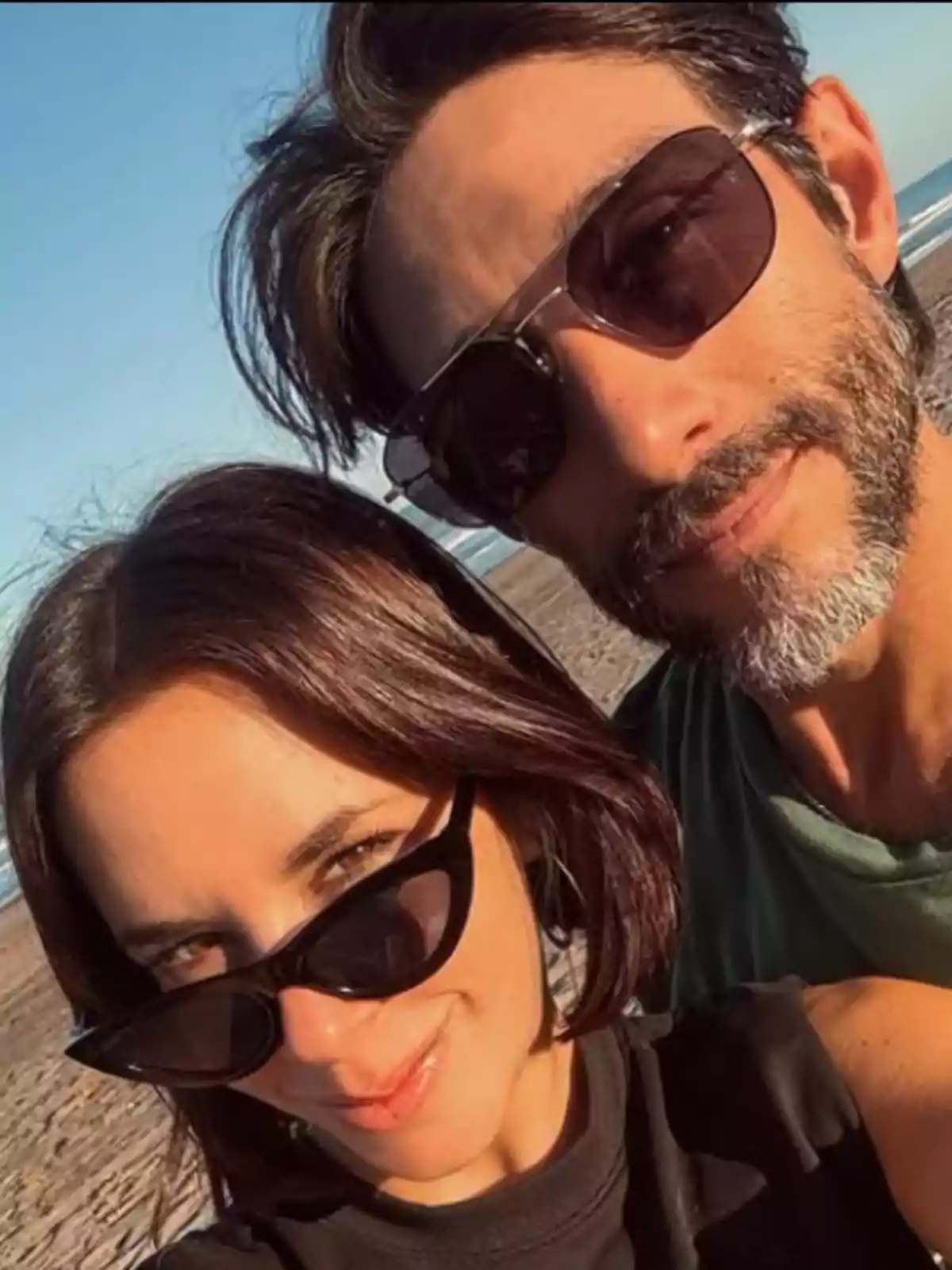 Couple taking a selfie on the beach wearing sunglasses and smiling under the sunset light Couple taking a selfie on the beach wearing sunglasses and smiling under the sunset light