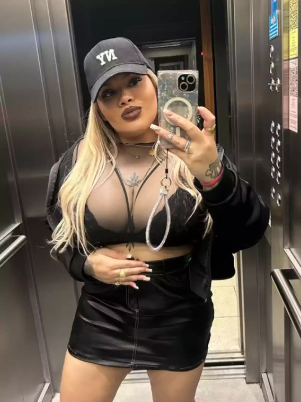Mujer rubia con gorra negra y falda de cuero tomándose una selfie en un ascensor Mujer rubia con gorra negra y falda de cuero tomándose una selfie en un ascensor