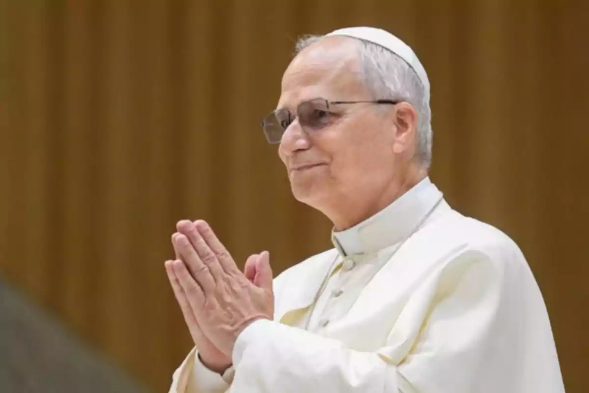 Hombre mayor con gafas y vestimenta religiosa blanca juntando las manos en actitud de oración