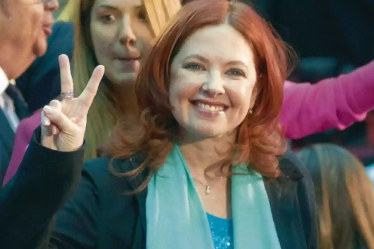 Mujer pelirroja sonriente haciendo la señal de la paz con los dedos en un evento público Mujer pelirroja sonriente haciendo la señal de la paz con los dedos en un evento público