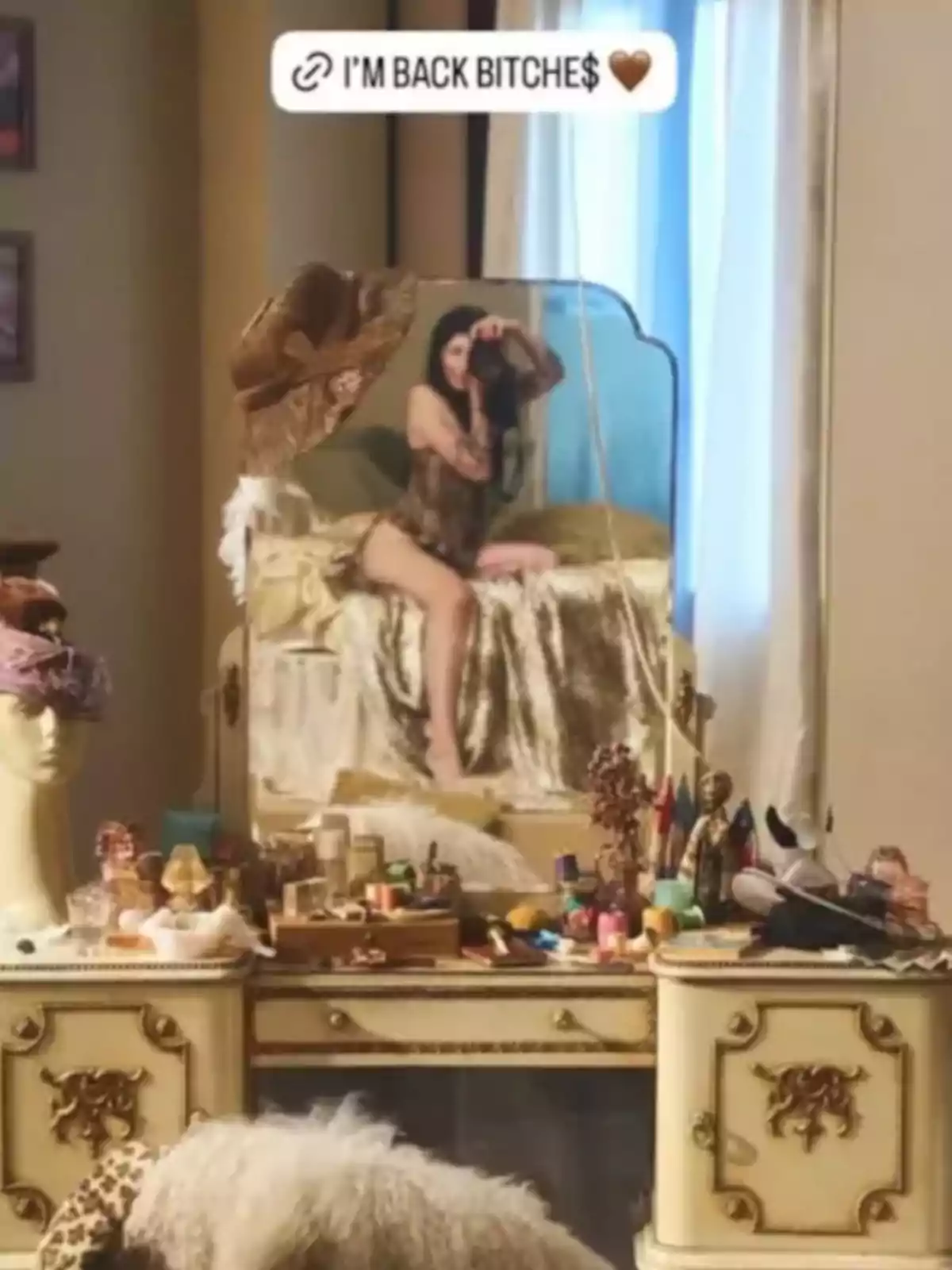 A woman is reflected in a mirror as she poses sitting on a bed, in front of an antique vanity filled with makeup and accessories, in a room decorated in vintage style. A woman is reflected in a mirror as she poses sitting on a bed, in front of an antique vanity filled with makeup and accessories, in a room decorated in vintage style.