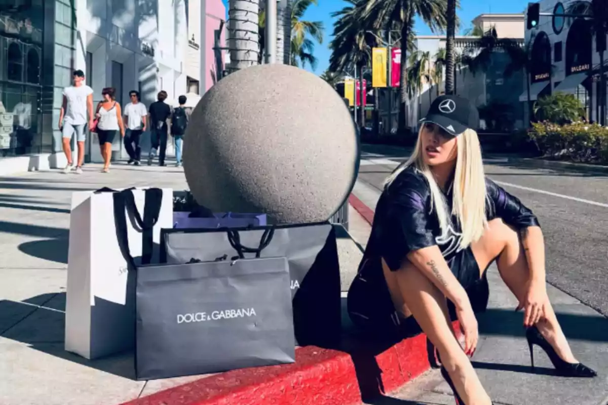 Blonde woman with a black cap sitting on the sidewalk next to several luxury brand shopping bags on a sunny street with palm trees and exclusive stores Blonde woman with a black cap sitting on the sidewalk next to several luxury brand shopping bags on a sunny street with palm trees and exclusive stores