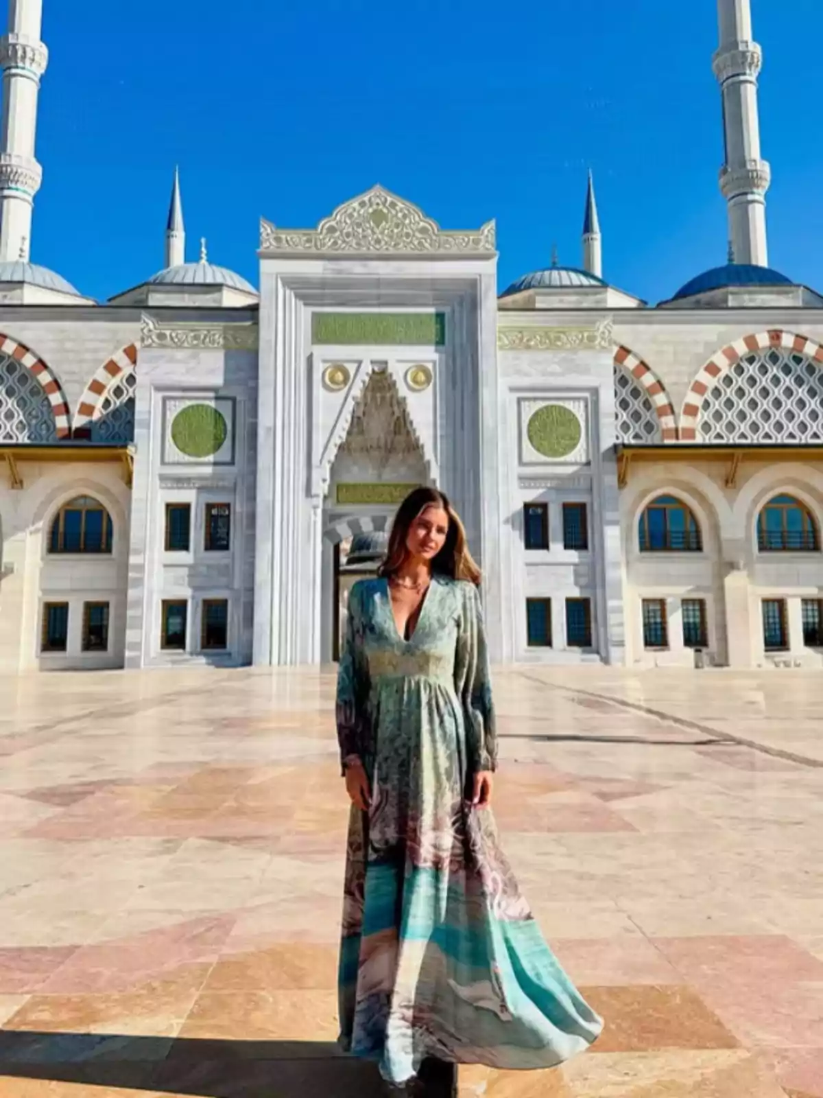 Woman in a long colorful dress posing in front of a mosque with a clear blue sky Woman in a long colorful dress posing in front of a mosque with a clear blue sky