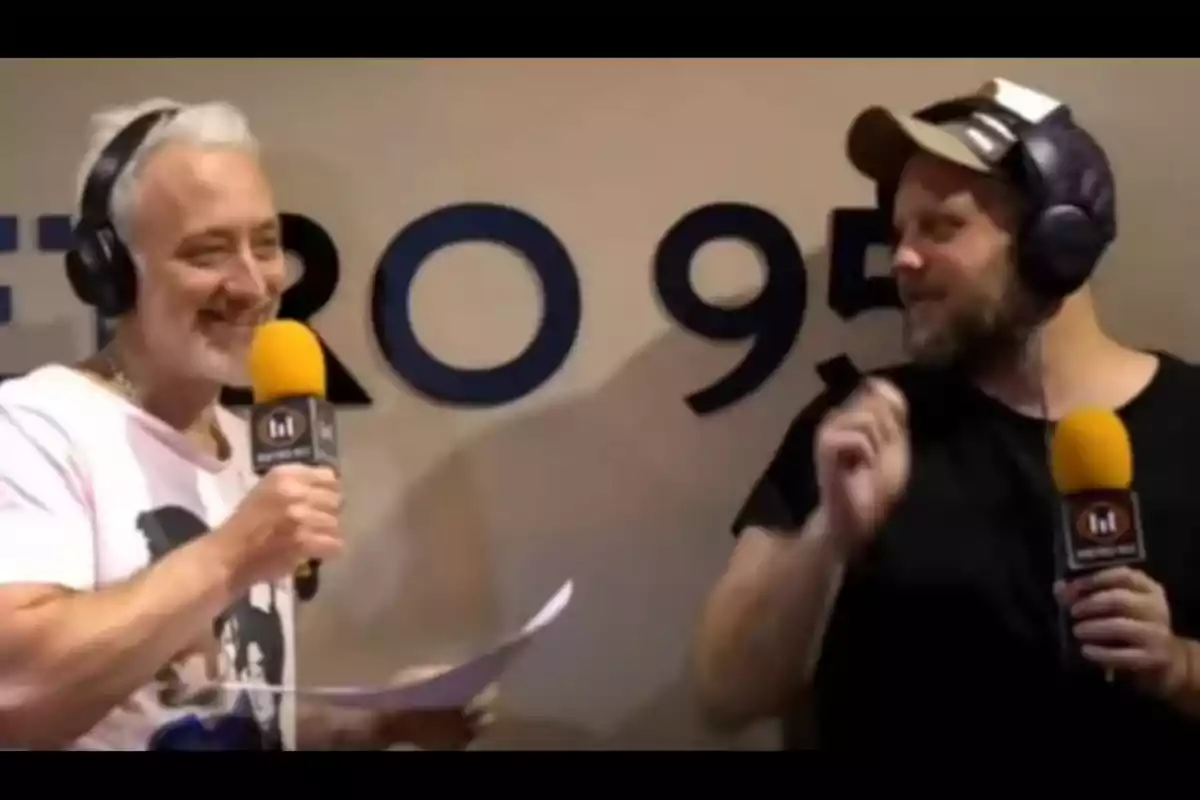 Dos hombres con micrófonos de radio y auriculares conversan y sonríen en un estudio con el logo de una emisora en la pared. Dos hombres con micrófonos de radio y auriculares conversan y sonríen en un estudio con el logo de una emisora en la pared.