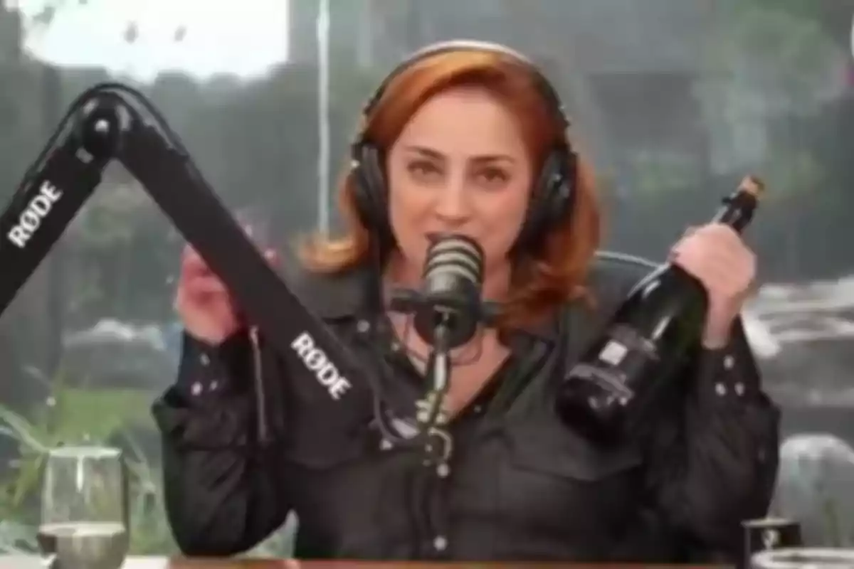 Red-haired woman with headphones speaking into a microphone while holding a bottle in a recording booth Red-haired woman with headphones speaking into a microphone while holding a bottle in a recording booth