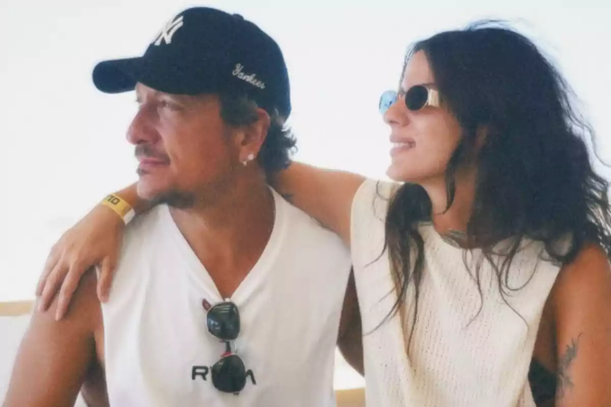 Two people sitting together, a woman wearing sunglasses and a man with a black cap, both looking relaxed and smiling.
