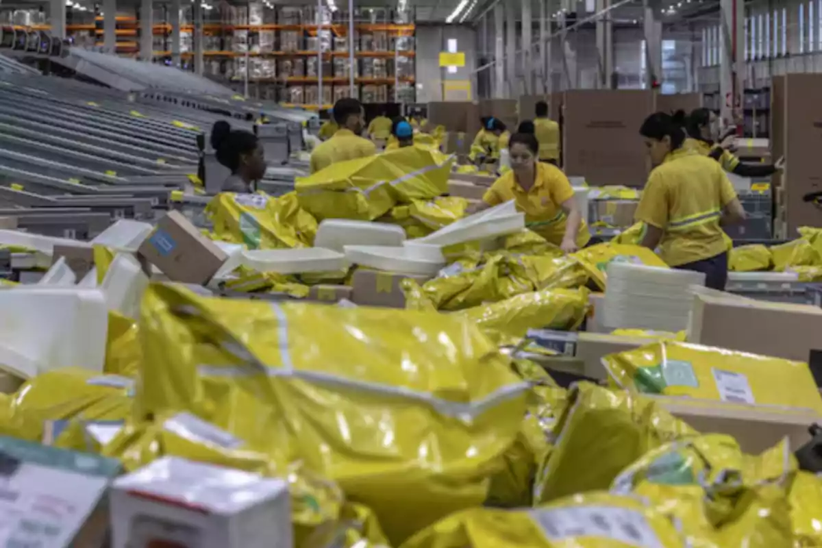 Trabajadores organizan paquetes en una bodega llena de bolsas y cajas amarillas Trabajadores organizan paquetes en una bodega llena de bolsas y cajas amarillas