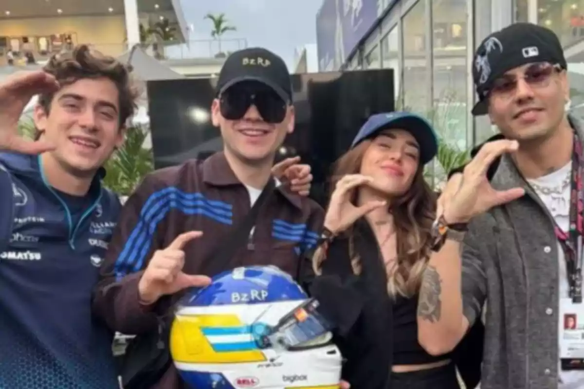 Cuatro personas posan sonrientes haciendo la letra C con la mano y una de ellas sostiene un casco de carreras azul y amarillo Cuatro personas posan sonrientes haciendo la letra C con la mano y una de ellas sostiene un casco de carreras azul y amarillo