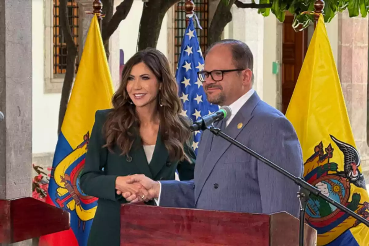 Two people shaking hands in front of microphones with the flags of Ecuador and the United States in the background