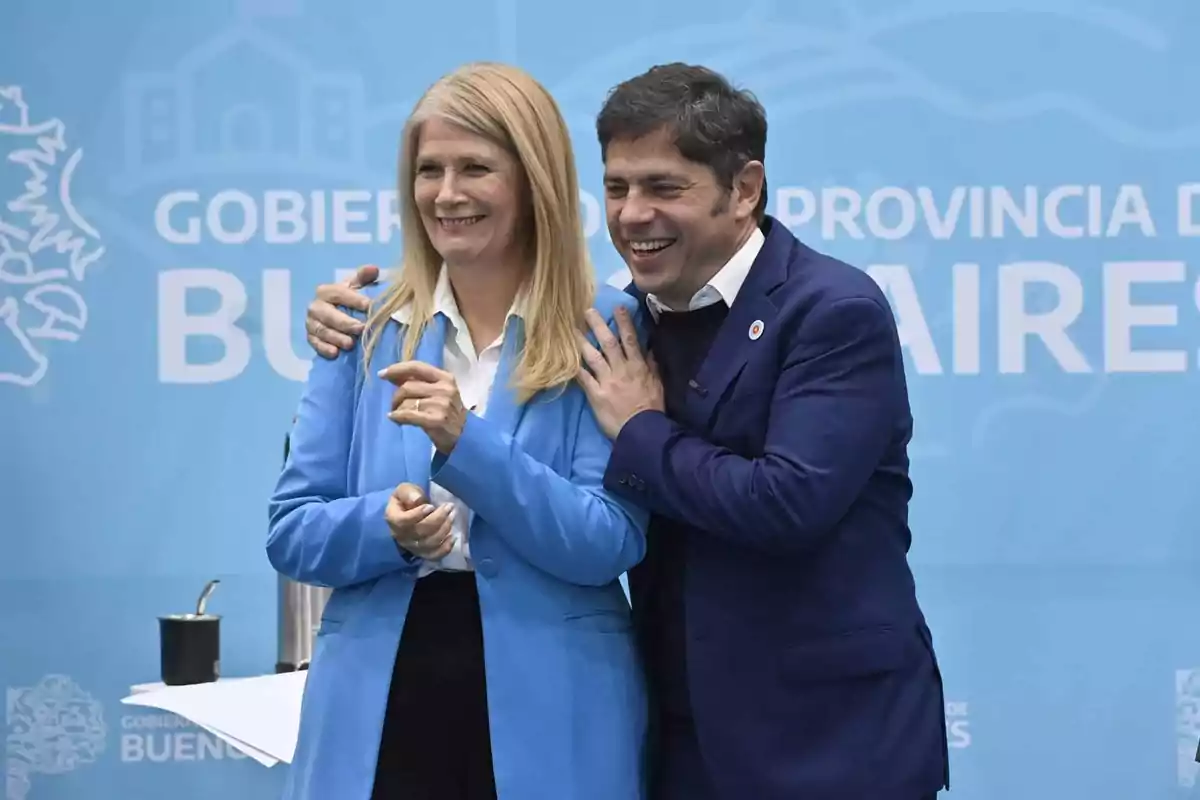 Two people smile and pose together in front of a blue background with white letters referring to the government of the province of Buenos Aires. Two people smile and pose together in front of a blue background with white letters referring to the government of the province of Buenos Aires.