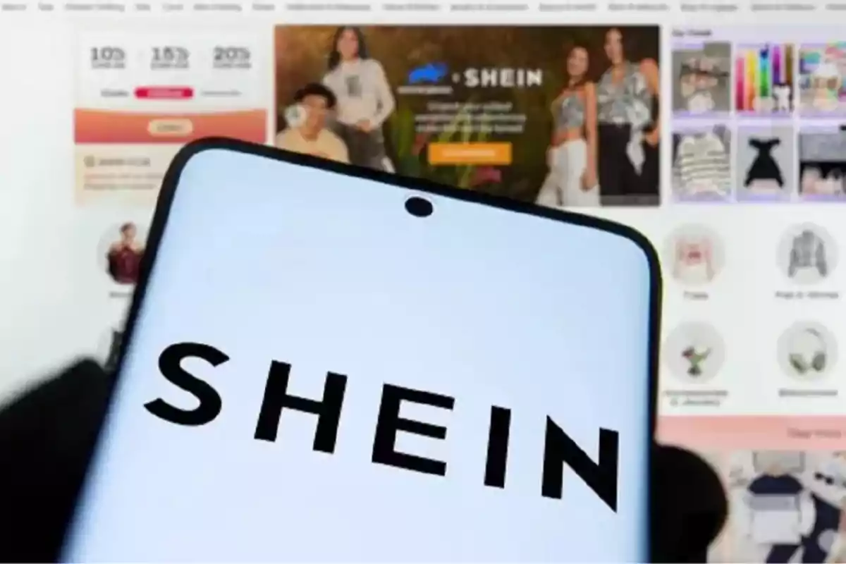 Person holding a mobile phone displaying the Shein logo in front of a computer with the Shein website open. Person holding a mobile phone displaying the Shein logo in front of a computer with the Shein website open.