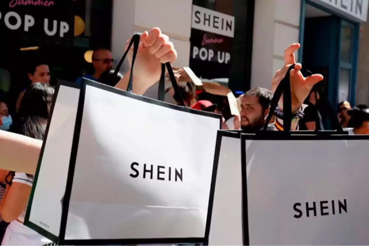 Personas sosteniendo bolsas de compras de la tienda Shein frente a una tienda pop up con varias personas alrededor