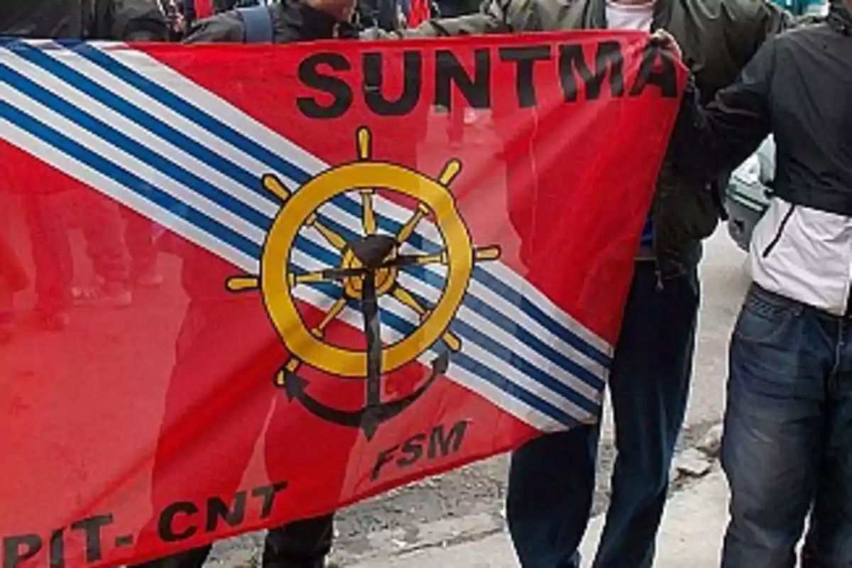 People hold a red flag with a yellow and blue helm in the center, light blue and white diagonal stripes, and the initials SUNTMA at the top.