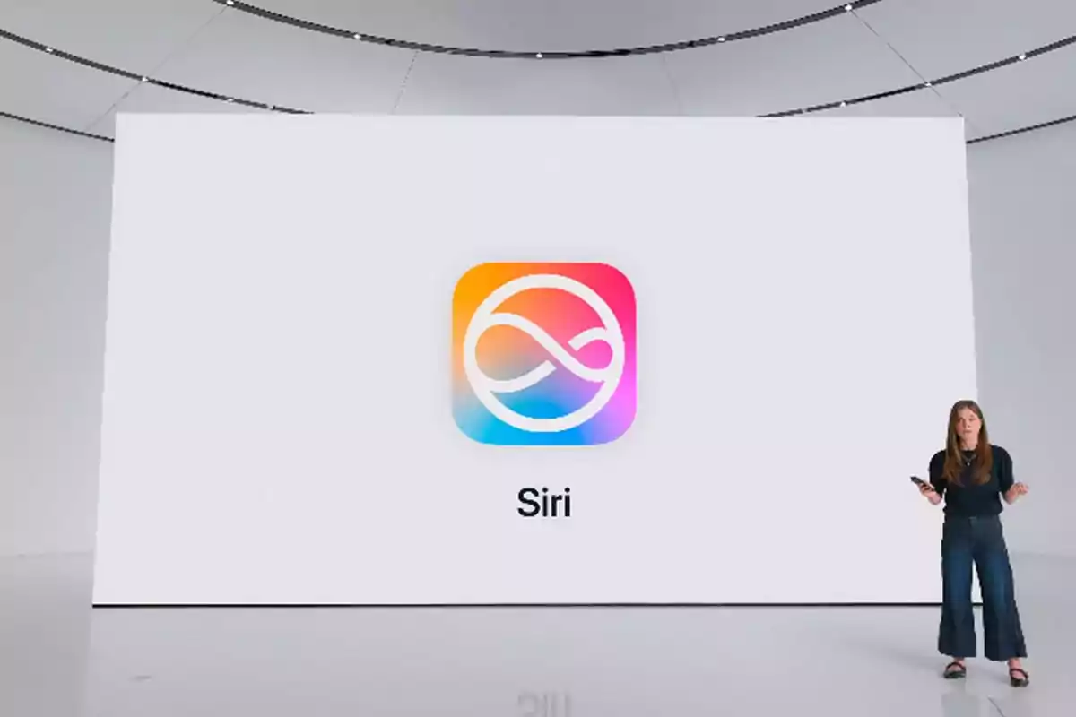 Una mujer presenta en un escenario frente a una pantalla grande que muestra el logo colorido de Siri y el nombre Siri debajo.