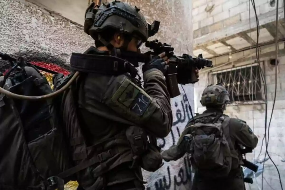 Armed soldiers with tactical gear advance down an urban street with concrete walls and graffiti.
