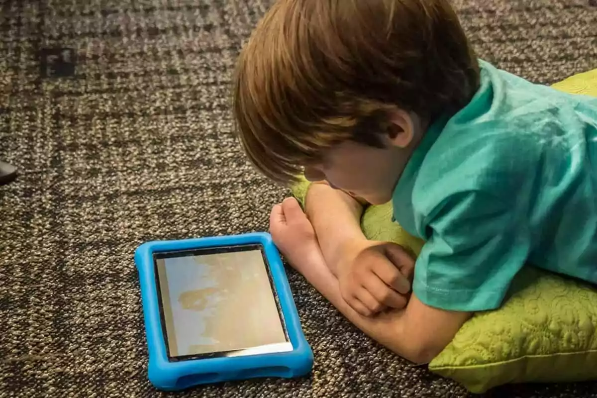 Child lying on the floor using a tablet with a blue case Child lying on the floor using a tablet with a blue case