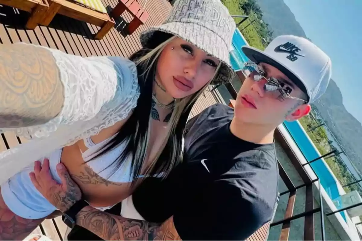 Pareja joven con tatuajes tomándose una selfie junto a una piscina al aire libre en un día soleado Pareja joven con tatuajes tomándose una selfie junto a una piscina al aire libre en un día soleado