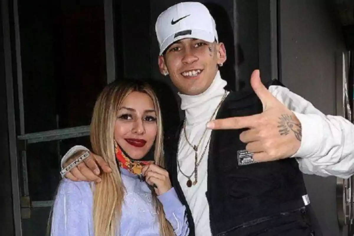 Two young people pose smiling for the camera, one of them wearing a white cap and the other with long blonde hair.