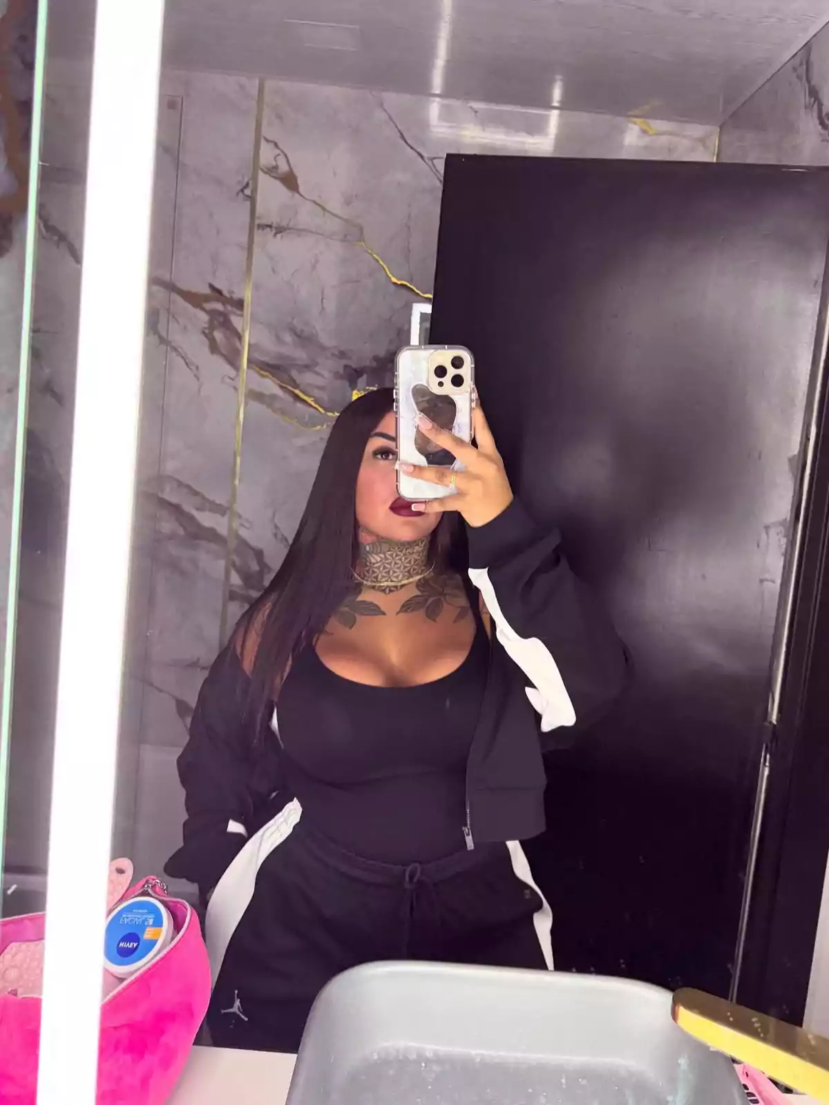 Mujer tomándose una selfie en el baño con ropa deportiva negra y fondo de mármol Mujer tomándose una selfie en el baño con ropa deportiva negra y fondo de mármol