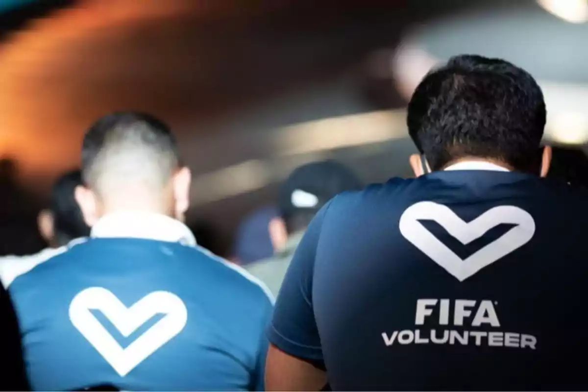 Personas de espaldas usando camisetas azules con el logo de voluntarios de la FIFA