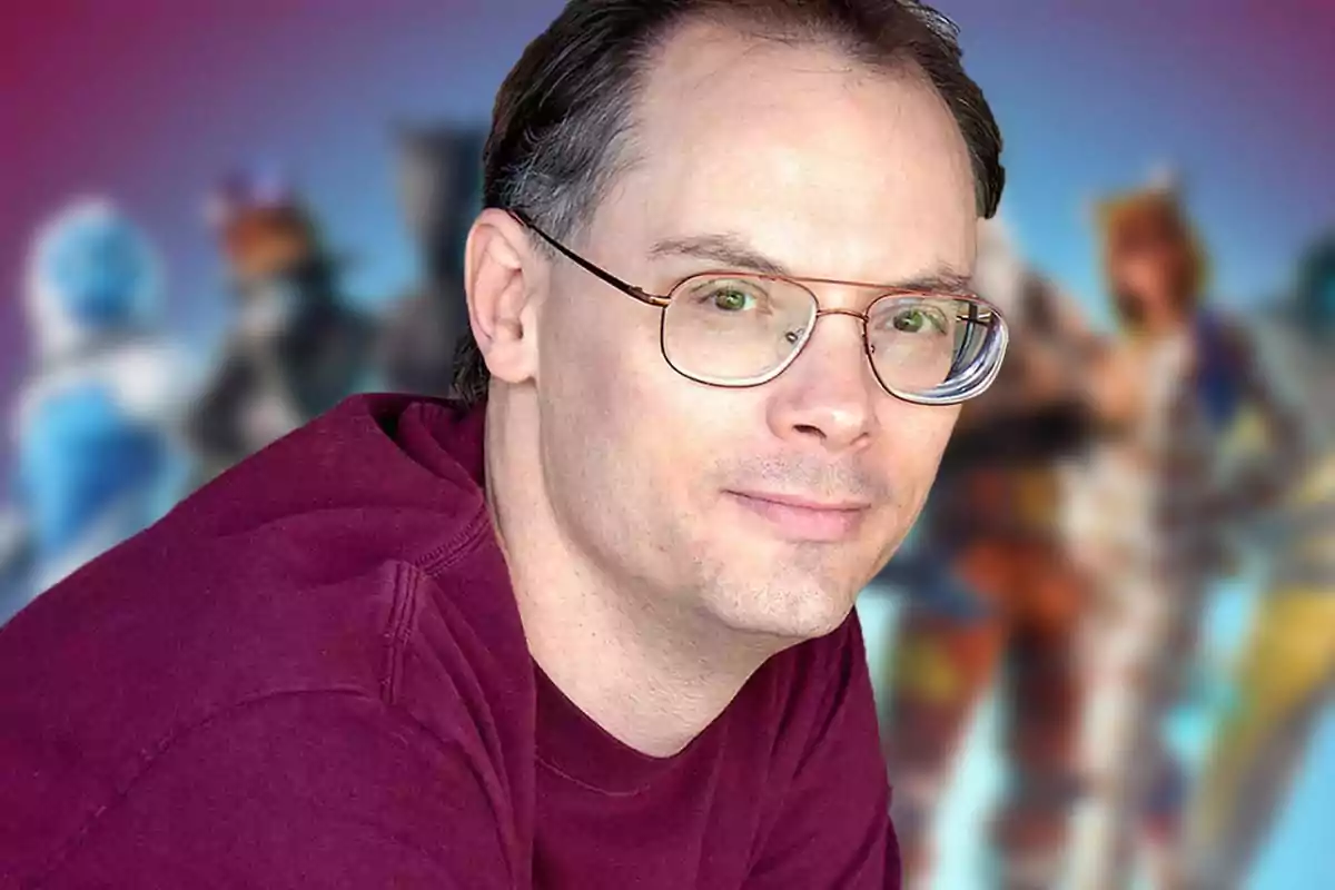 Hombre con gafas y camiseta burdeos posando frente a un fondo colorido y desenfocado con figuras de personajes. Hombre con gafas y camiseta burdeos posando frente a un fondo colorido y desenfocado con figuras de personajes.