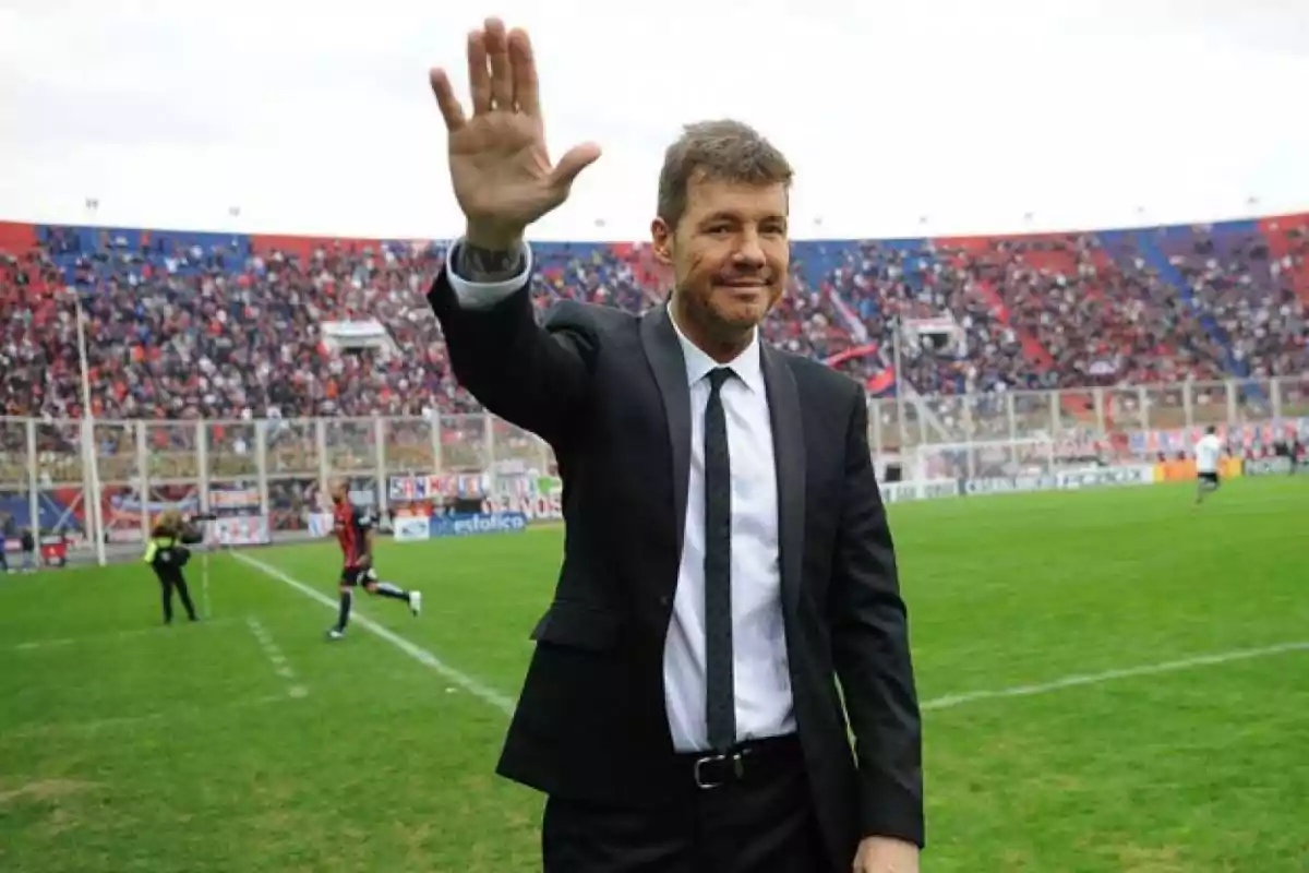 Man in a suit waving in a football stadium full of spectators