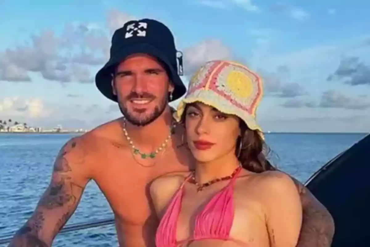 Pareja joven en traje de baño posando en un bote con el mar y el cielo azul de fondo ambos usando sombreros